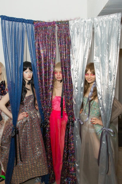 Three models posing in a silver, pink and green dress Backstage at the Matty Bovan fashion show