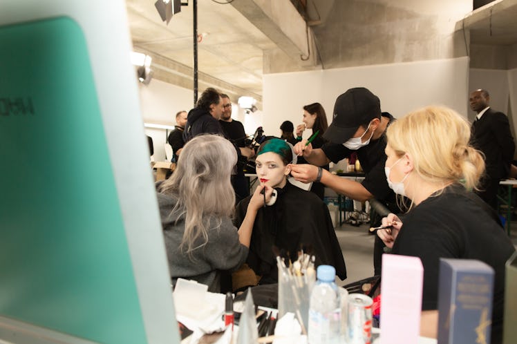Makeup and hair artists preparing a female model with black and green hair for a runway walk