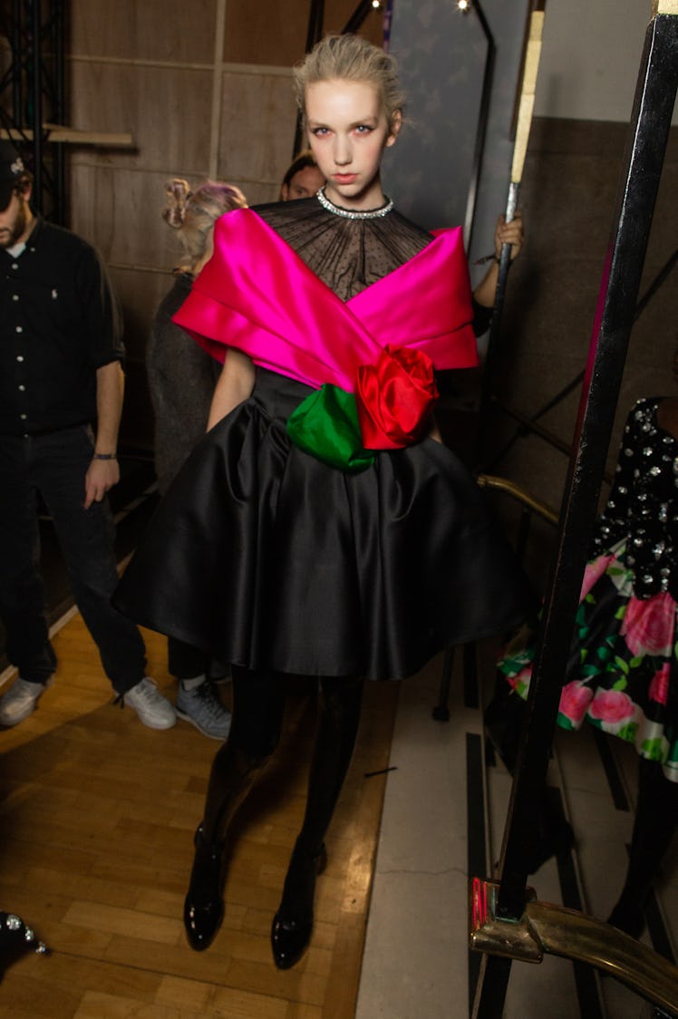 A model wearing a black dress with a pink detail and oversized red rose at Richard Quinn‘s fall coll...