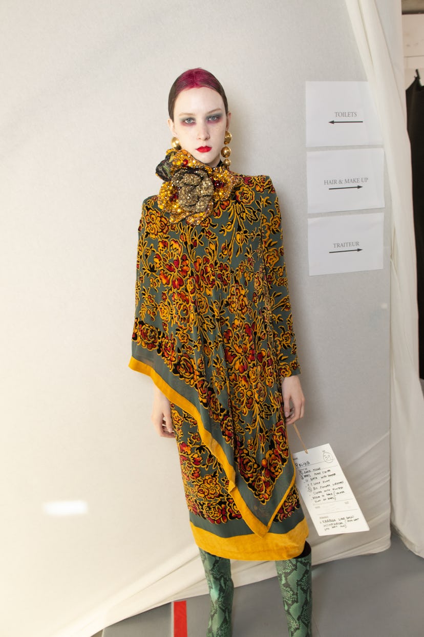 A model wearing an orange-green floral cape dress in backstage at Dries Van Noten