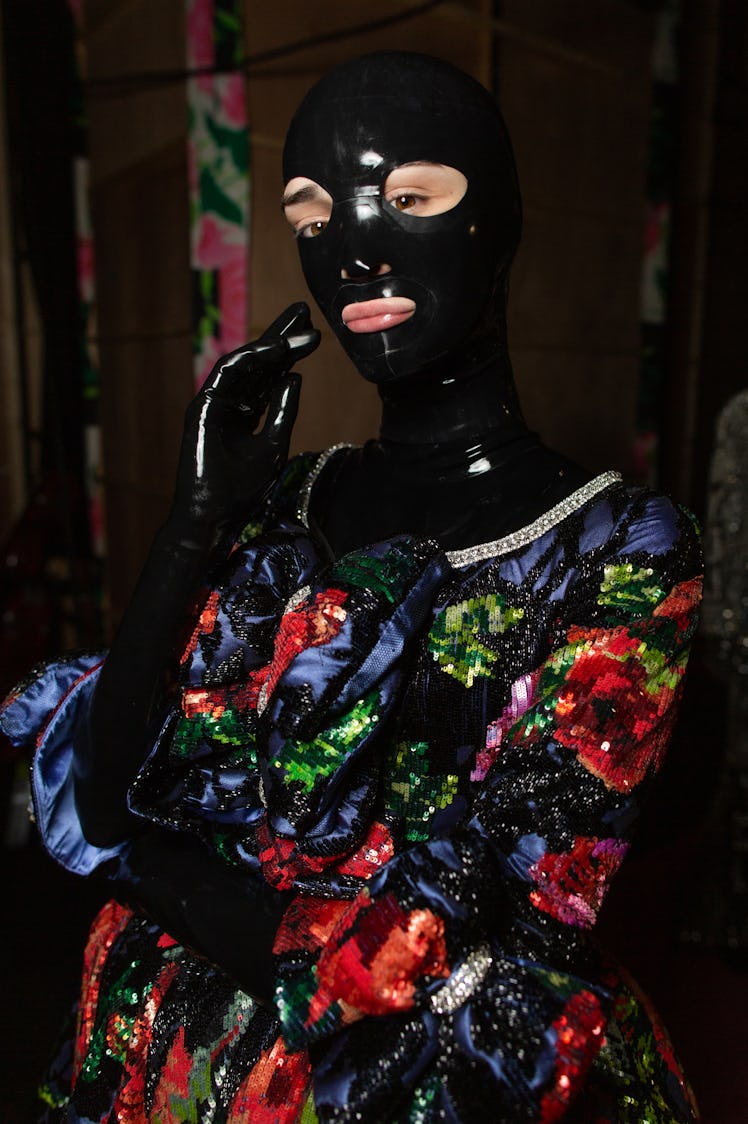 A model wearing a red-green-blue satin dress with a black latex face mask at Richard Quinn‘s fall co...