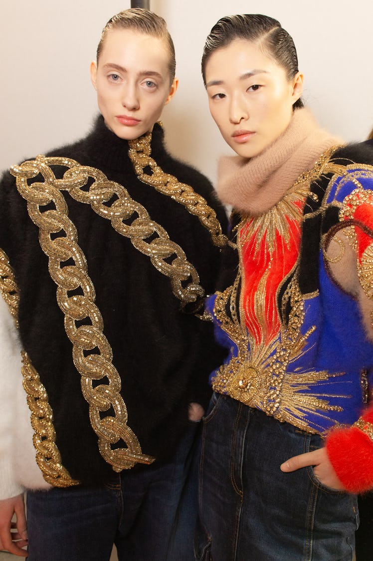 A model in a black-gold sweater and a model in a blue-red sweater backstage at Balmain Fall 2020