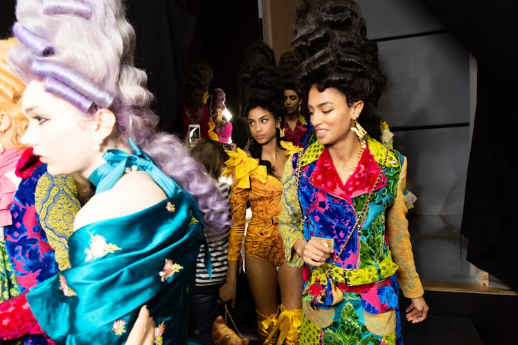 Several models in multi-colored dresses and coats walking backstage at the Moschino Fall 2020 show