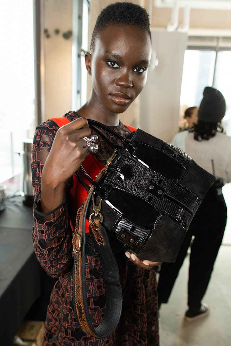 A short-haired female model posing while holding a black bag