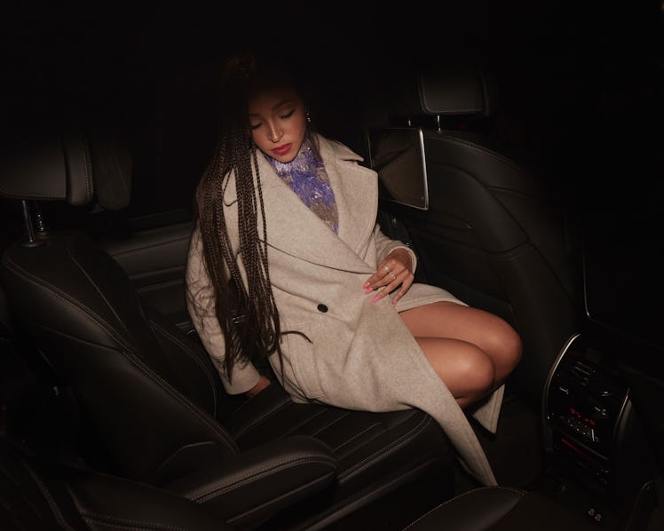 Tinashe sitting in a car while wearing a white coat
