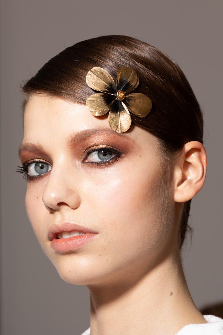 Close up of female model wearing a golden flower hair clip and a sleek bun hairstyle