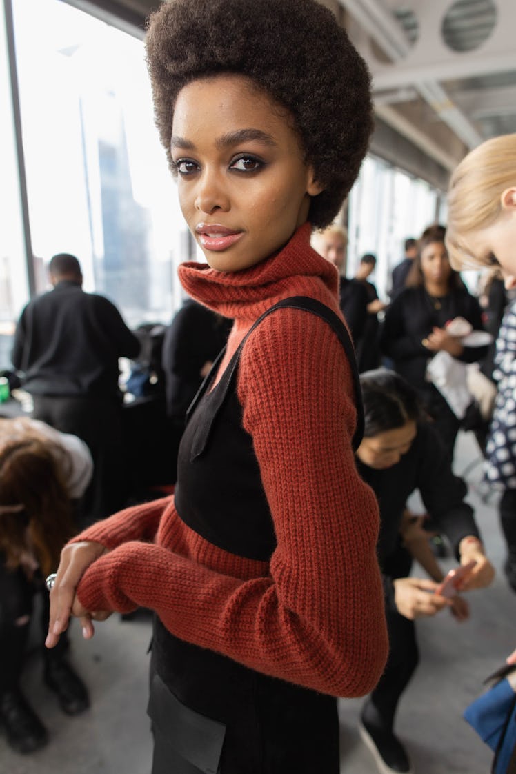 A curly-haired model posing for a photo while wearing a red sweater and a black top over it