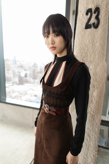 A black-haired female model posing while wearing a brown top and skirt combination