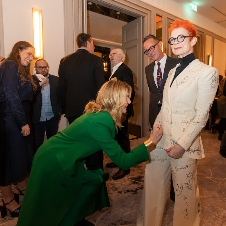 Sandy Powell taking a signature from Laura Dern on her white suit costume