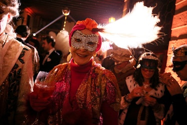 A woman holding a glass in a red dress, wearing a black and white mask at the Save Venice party
