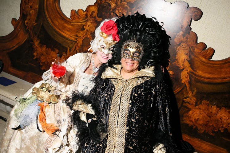 Two women smiling and wearing Venetian masks and traditional gowns inside the Save Venice party