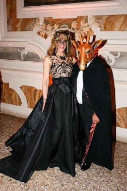 A man with a giraffe mask and a woman with a floral veil mask dressed up in a coat and gown for the ...