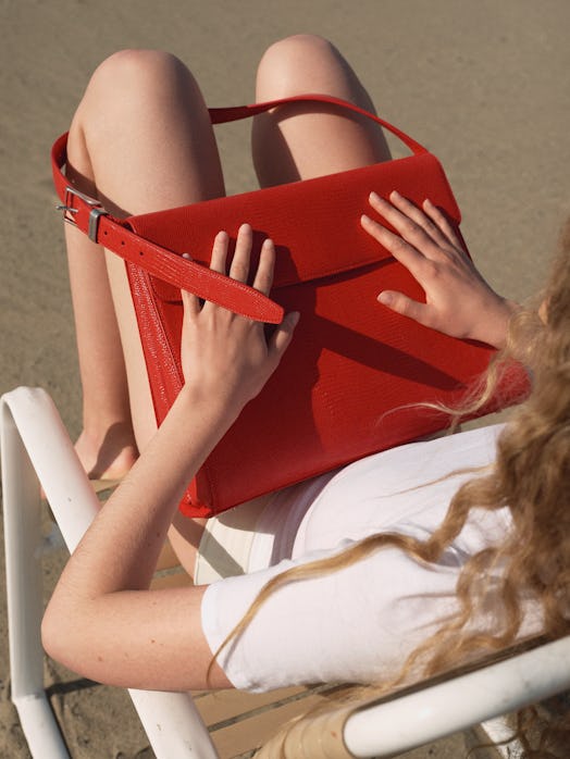 A woman sitting while wearing a white t-shirt and holding a red Balenciaga bag on her lap
