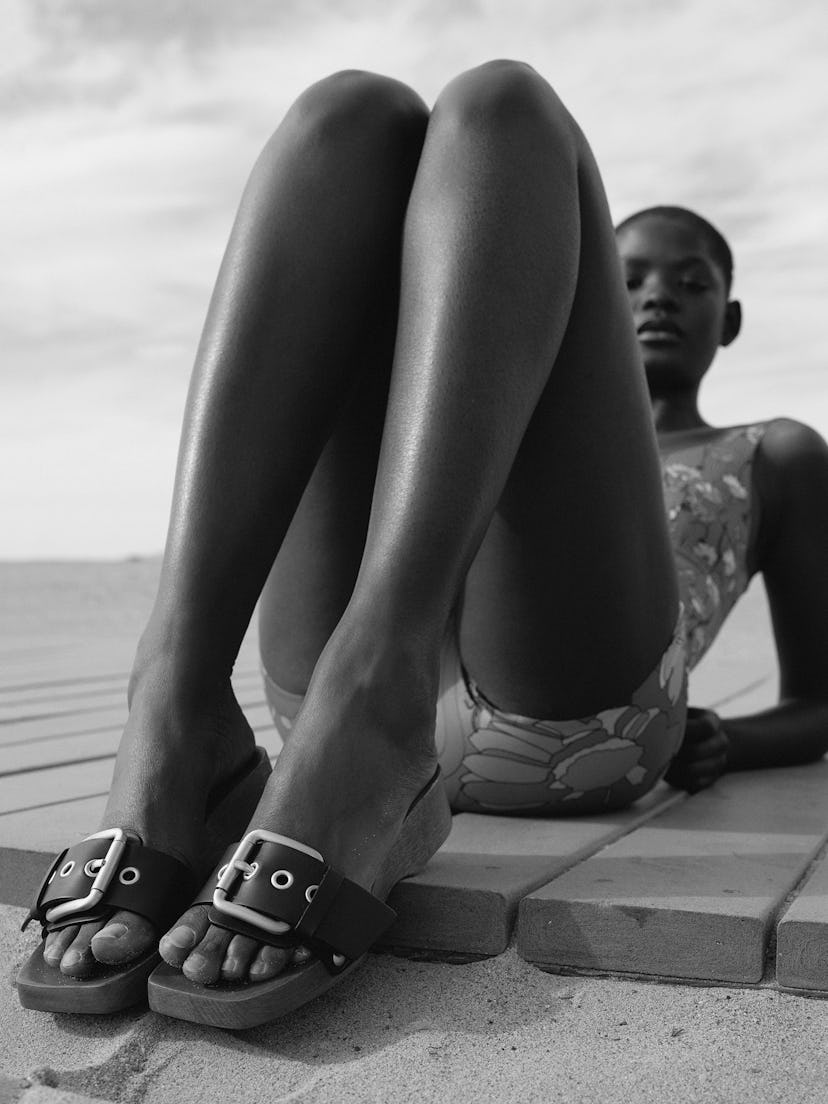 A model wearing designer flat leather slippers with a metal buckle for spring