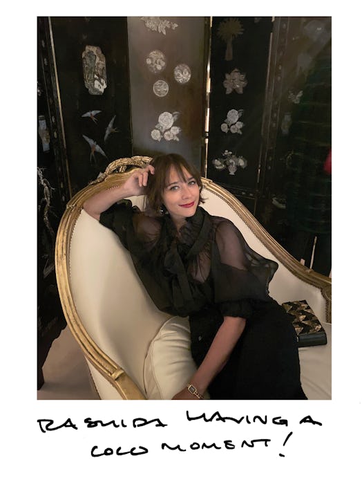 Rashida Jones in a black Chanel gown sitting, posing and smiling on a beige armchair