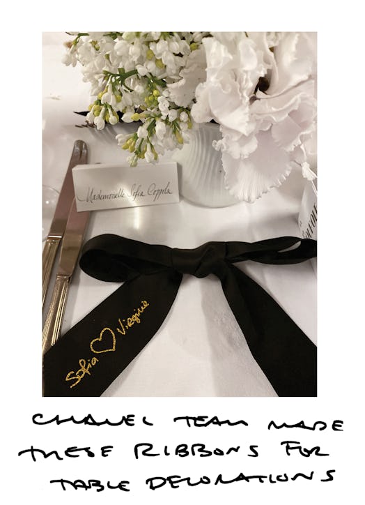 A large black Chanel ribbon decoration a table next to white flowers and a name plaquette for Sofia ...
