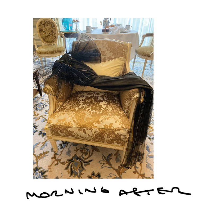 A black Chanel dress with a large tulle bow over a beige-golden chair
