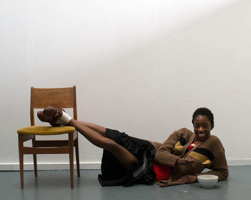 A woman holding her legs on a chair while sitting on the floor and eating from a bowl