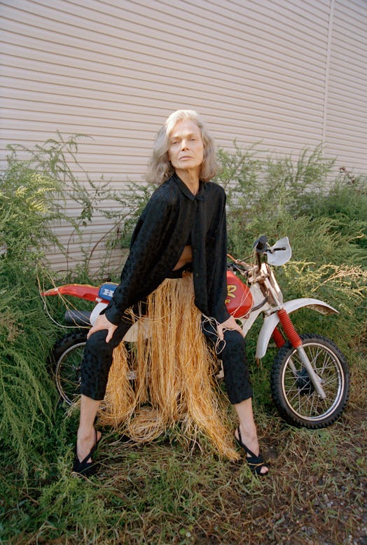 An older female model posing in a golden fringe skirt over black pants and a black jacket in front o...