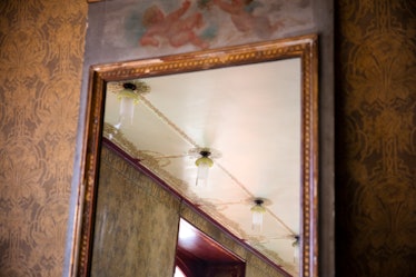 A large mirror with a gold frame on a wall with brown wallpaper inside Olivier Theyskens’s Paris Stu...