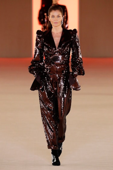 Helena Christensen walking down a runway in a sequined Versace jumpsuit