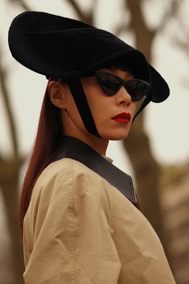 A woman posing in a white blazer and black hat