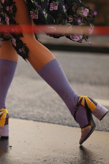 Legs of a woman that is walking while wearing purple socks and yellow-black heels