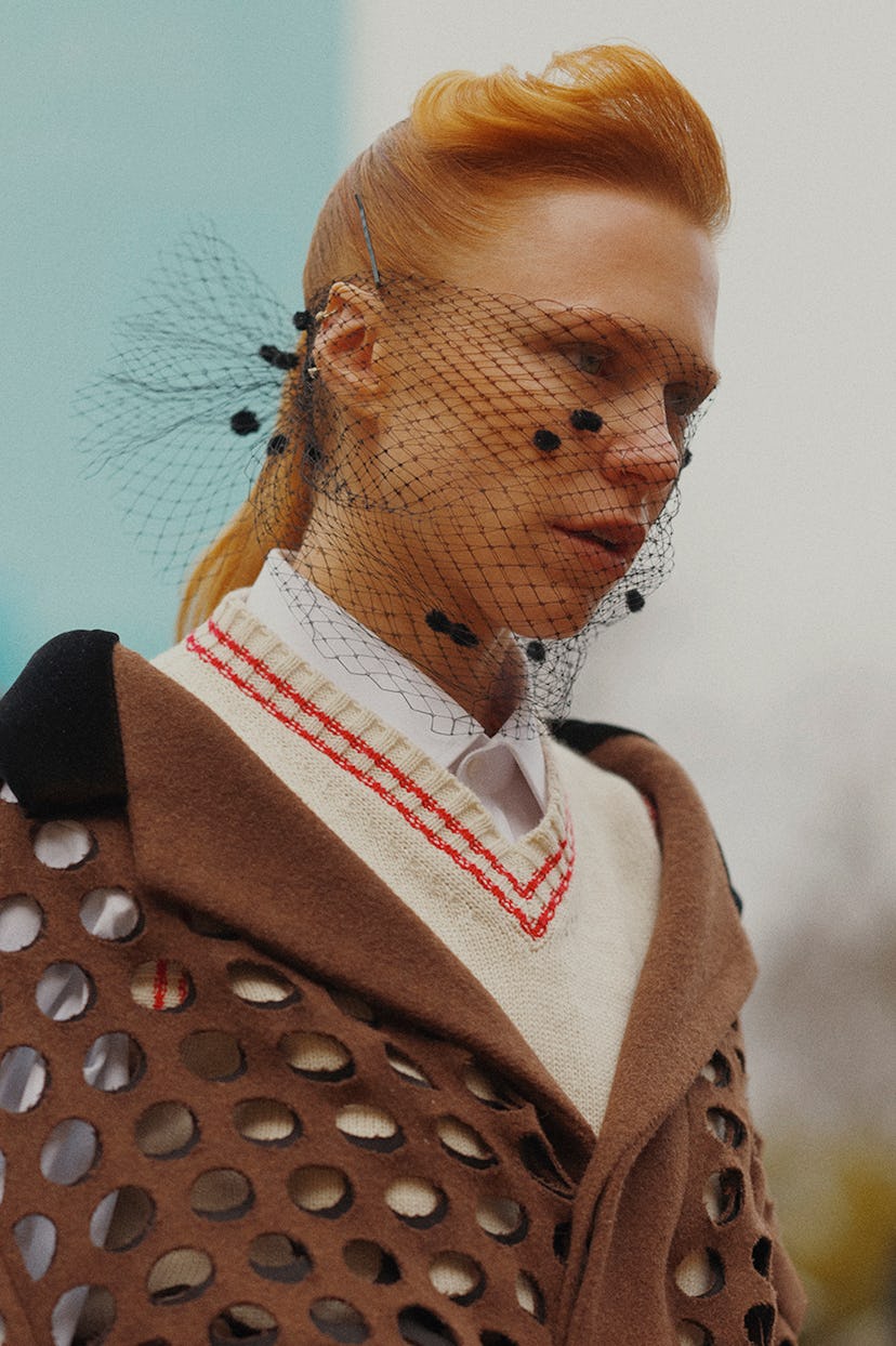A model at Paris Fashion week in a beige sweater, brown coat, and a black veil-like net on her face