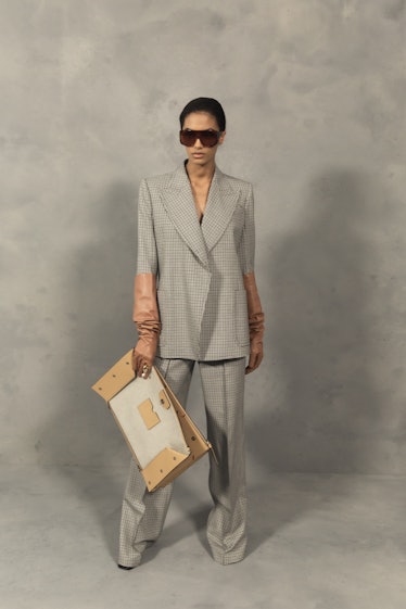 A model in a a grey suit, brown glove and a beige-brown bag backstage at the Givenchy Fall 2020
