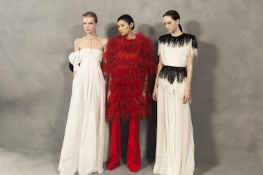 A model in a white dress, red feather dress, and a black-white dress backstage at the Givenchy Fall ...