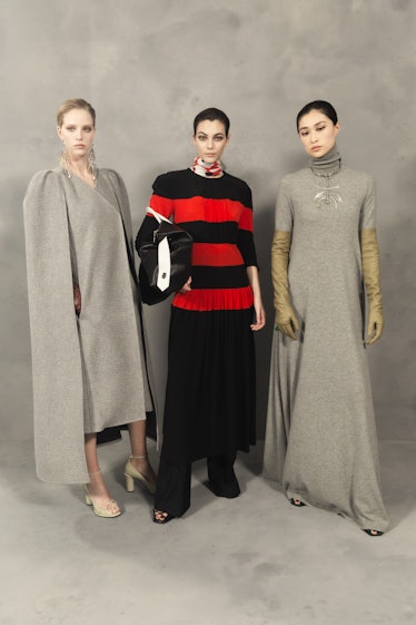 Two models in different-shaped grey dresses and a model in a black-red sweater and black pants