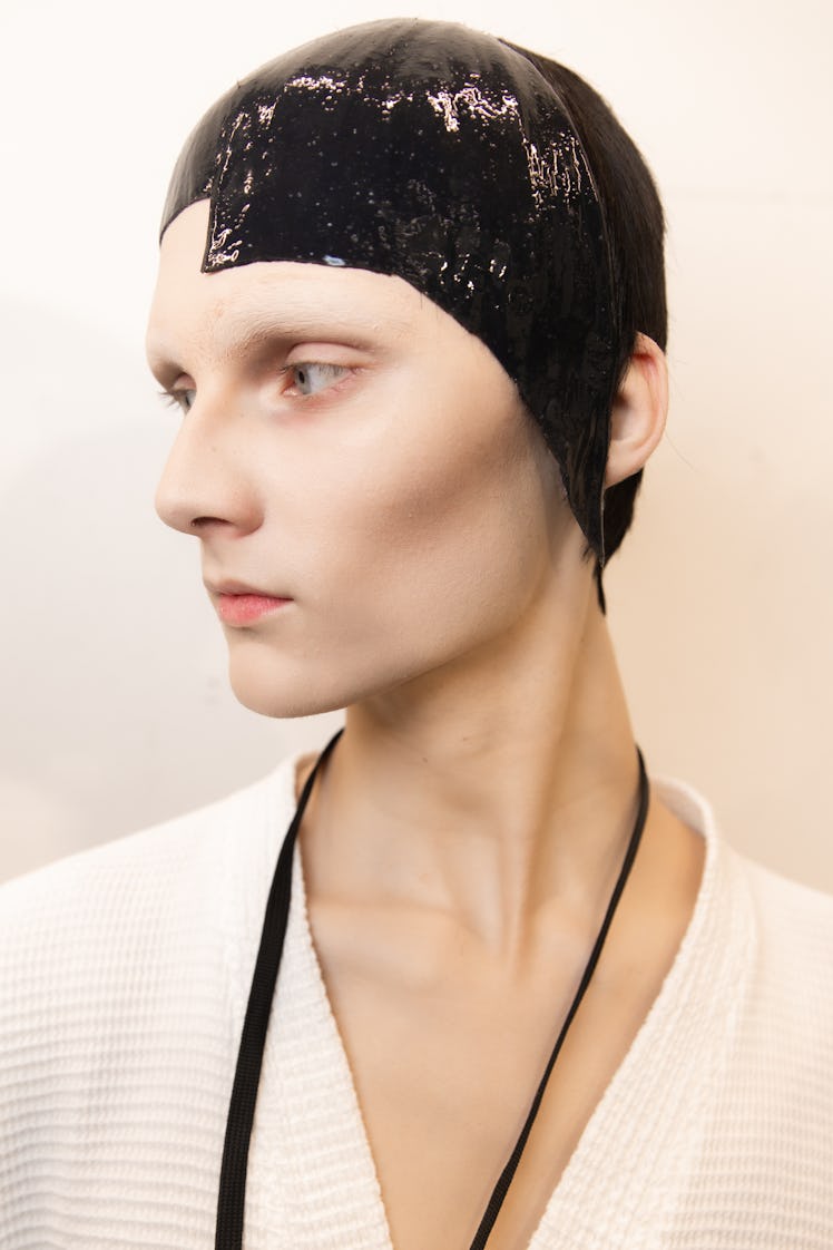 A model backstage at the Thom Browne fall 2020 show in a white robe and her hair slicked down, looki...