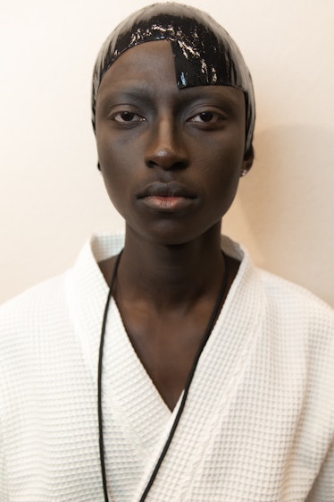 A model backstage at the Thom Browne fall 2020 show in a white robe and her hair slicked down, looki...