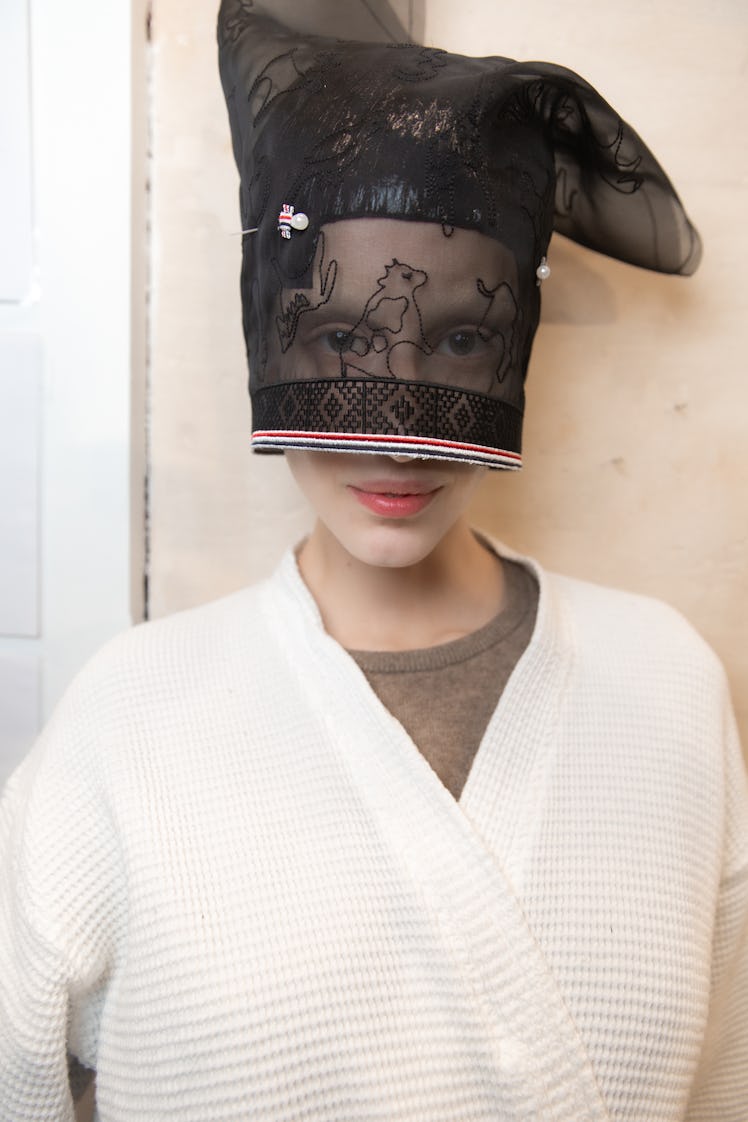 A model backstage at Thom Browne's fall 2020 show in a white robe and a black lace headpiece 