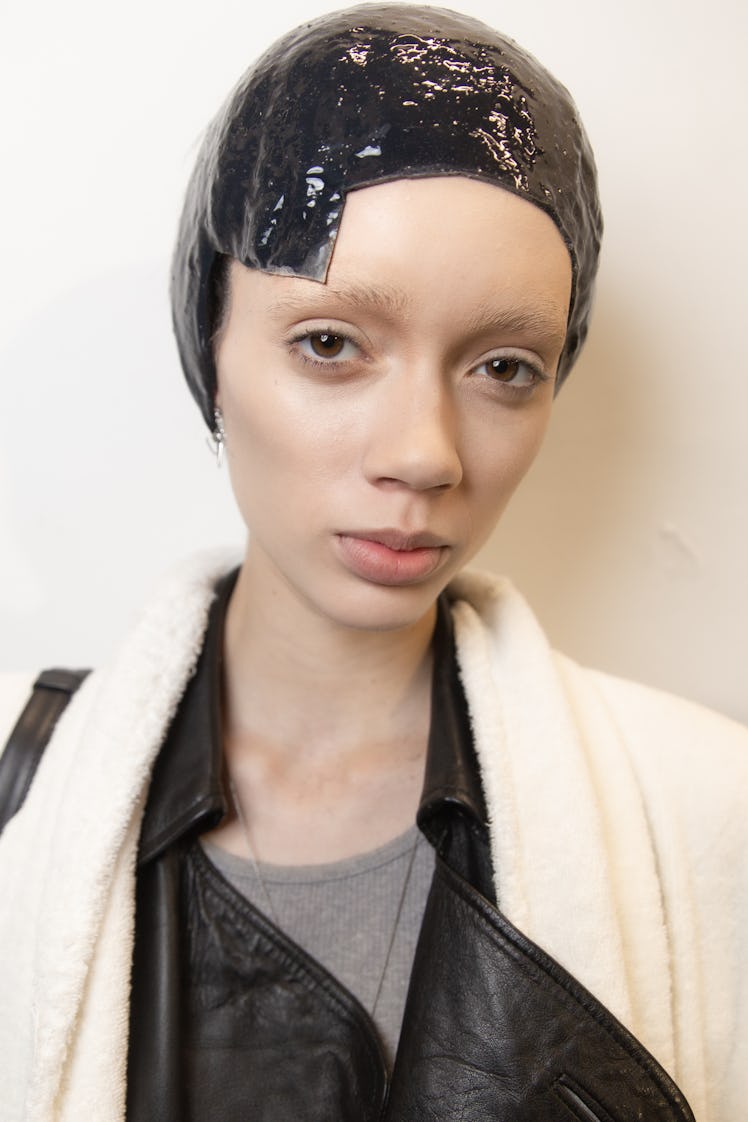 A model backstage at Thom Browne's fall 2020 show in a black leather jacket with a white robe over i...