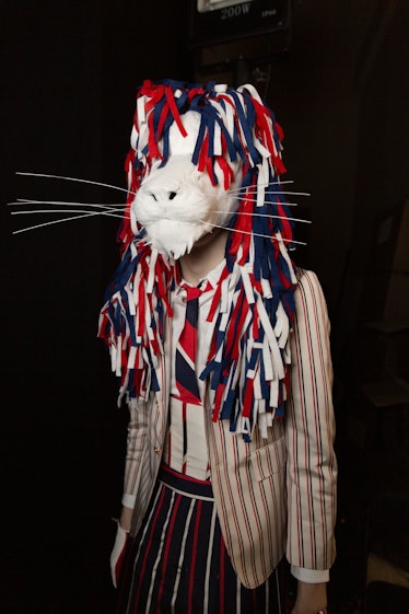 A model backstage at Thom Browne's fall 2020 show wearing a white tiger face mold and a blue, red an...