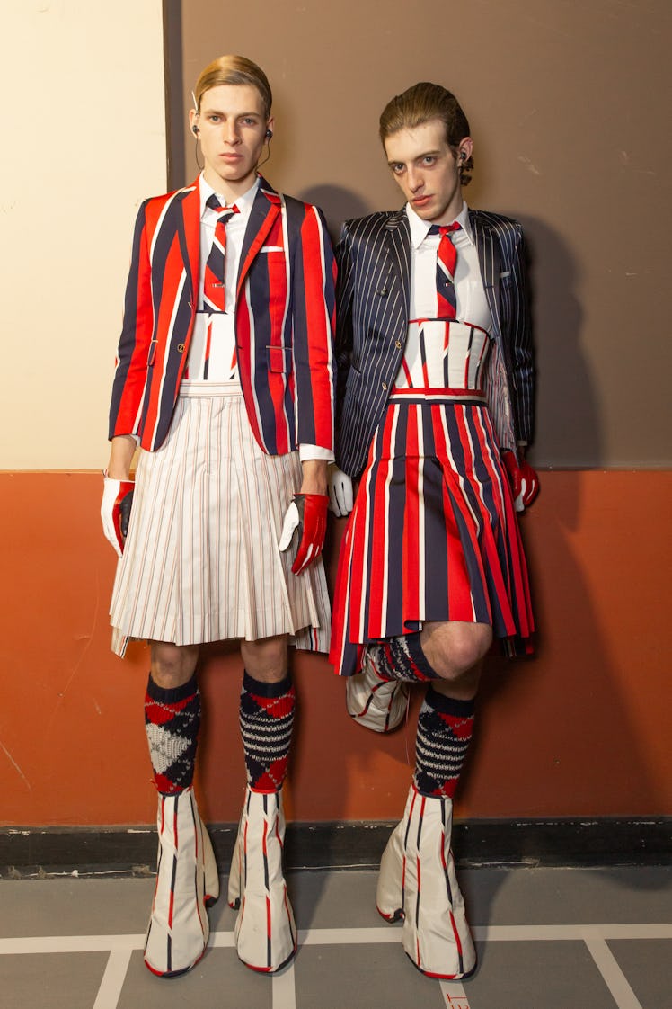 Two models backstage at Thom Browne's fall 2020 show in red, blue and white socks, blazer and skirt ...