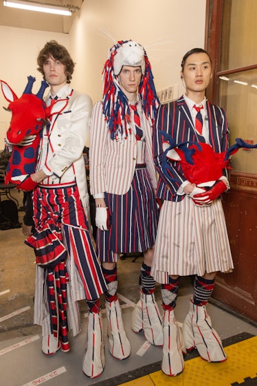 Two models backstage at Thom Browne's fall 2020 show in red, blue and white pants, skirt and blazer ...