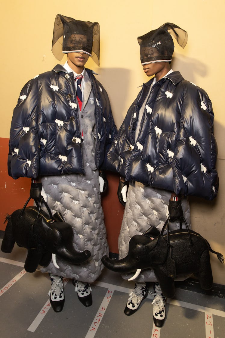 Two models at Thom Browne's show in black puffer coats, grey puffer dresses, black elephant bags and...