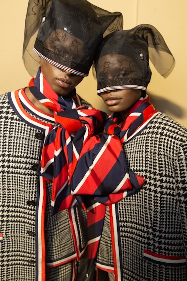 Two models backstage at Thom Browne's show in grey plaid jackets with red, white and blue  scarves, ...