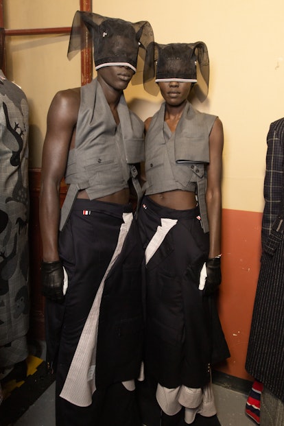 Two models in grey waistcoats, black skirts, and hats wearing Thom Browne at the Paris Fashion Week