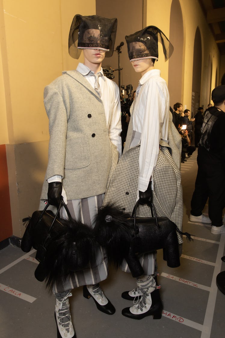 Two models backstage at Thom Browne's fall 2020 show in beige blazers, white shirt, lion-shaped bags...