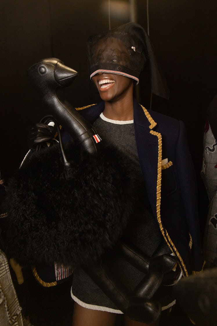 A model backstage at Thom Browne's fall 2020 show in a navy blue blazer with golden lining, a lace h...