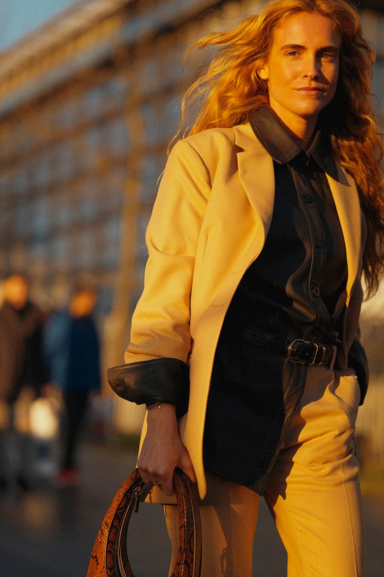 A woman walking while waring a white blazer, white pants, and a black shirt 