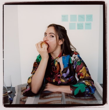 A portrait of Catherin Cohen sitting in a floral top and biting into an apple