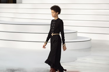 A model walking in a black skirt and a gold belt at the Chanel fall 2020 show