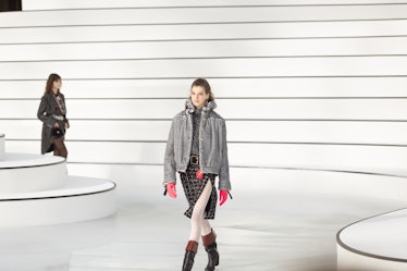 A model walking in a grey jacket, black skirt and brown boots at the Chanel fall 2020 show