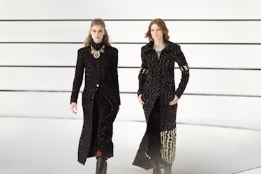 Two models sporting long black coats and walking at the Chanel fall 2020 show