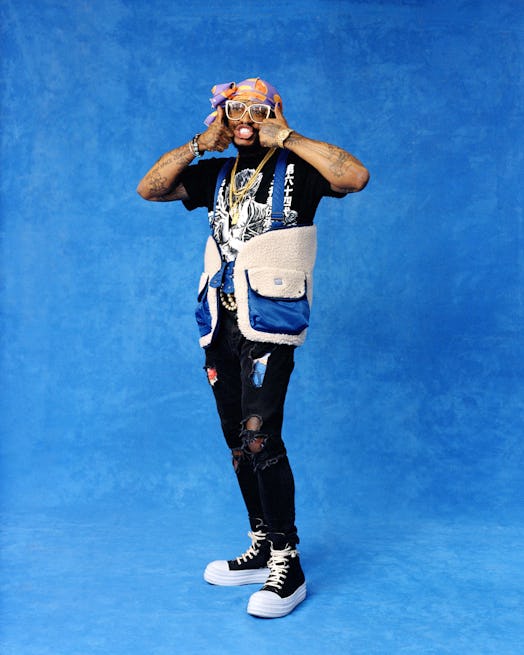Thundercat posing wearing a fun outfit with a bright blue background behind him.