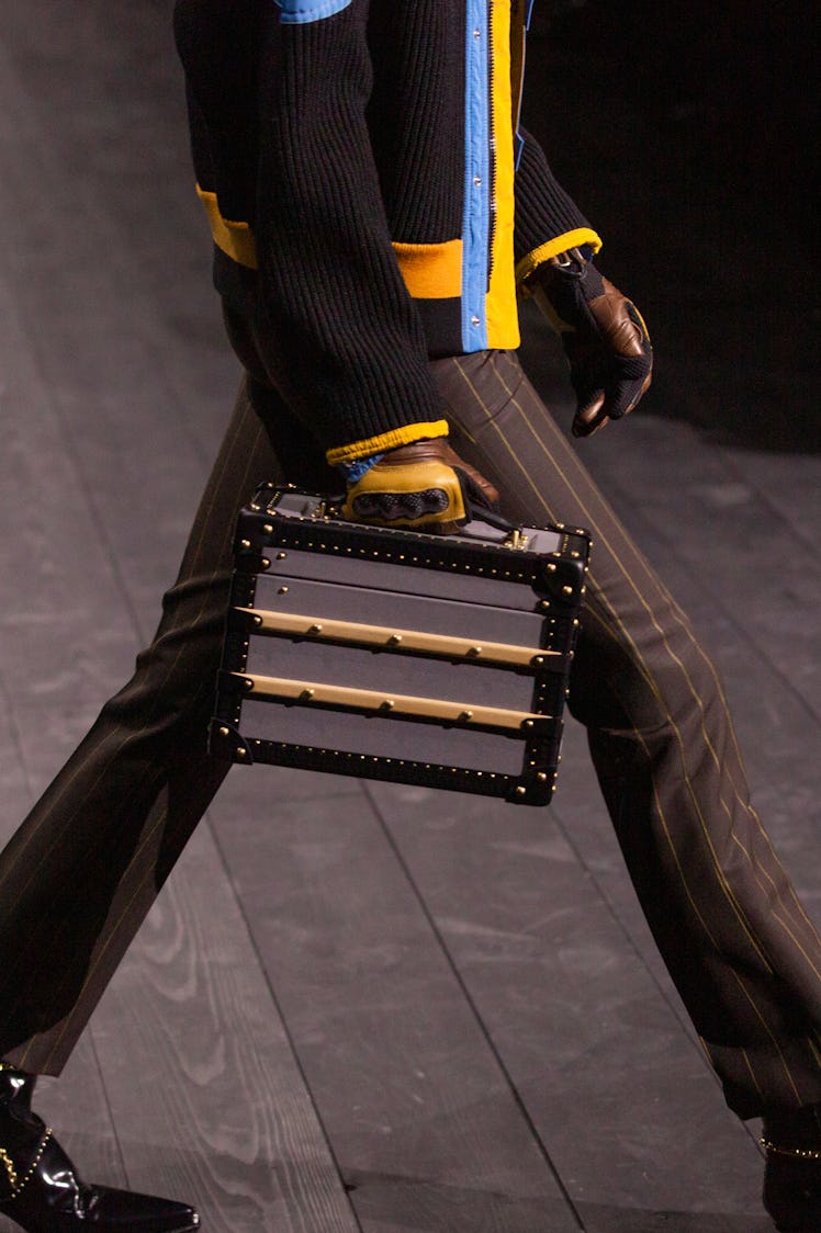 A model in a black-yellow-blue jacket and brown striped trousers and a black bag at the Louis Vuitto...